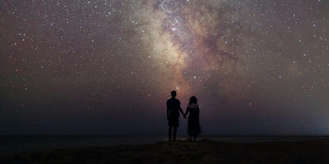 Couple walking near the sea at night under the starry sky