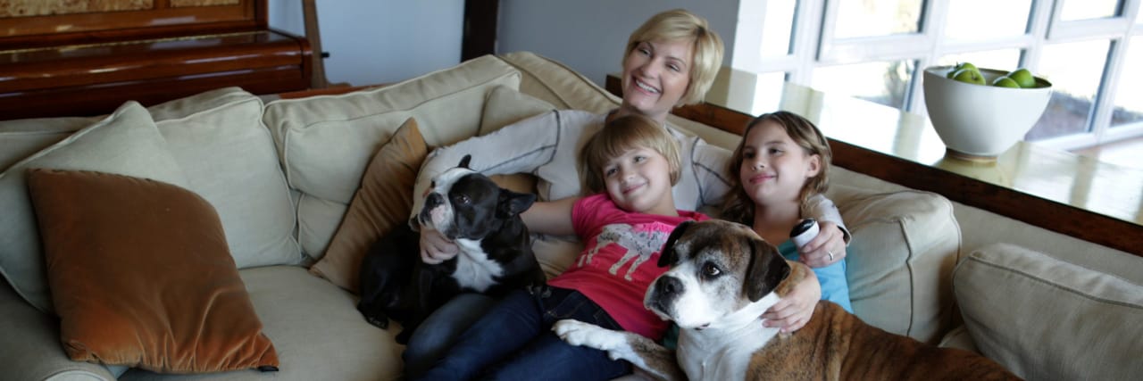 Explaining Parkinson's Disease to My Children Mother and daughters sitting on sofa with pets dogs, watching TV together.