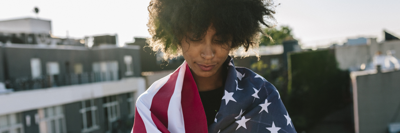 Why I'm Not Celebrating the 4th of July as a Woman With Chronic Illness Sad woman wrapped in American flag.