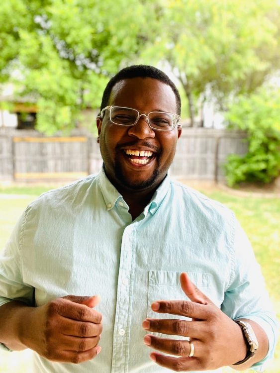 Sinclair, a Black man with glasses standing outside laughing