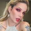 Halsey looking into the camera sporting bright eyeshadow and a lipstick in a white top with their hair up.