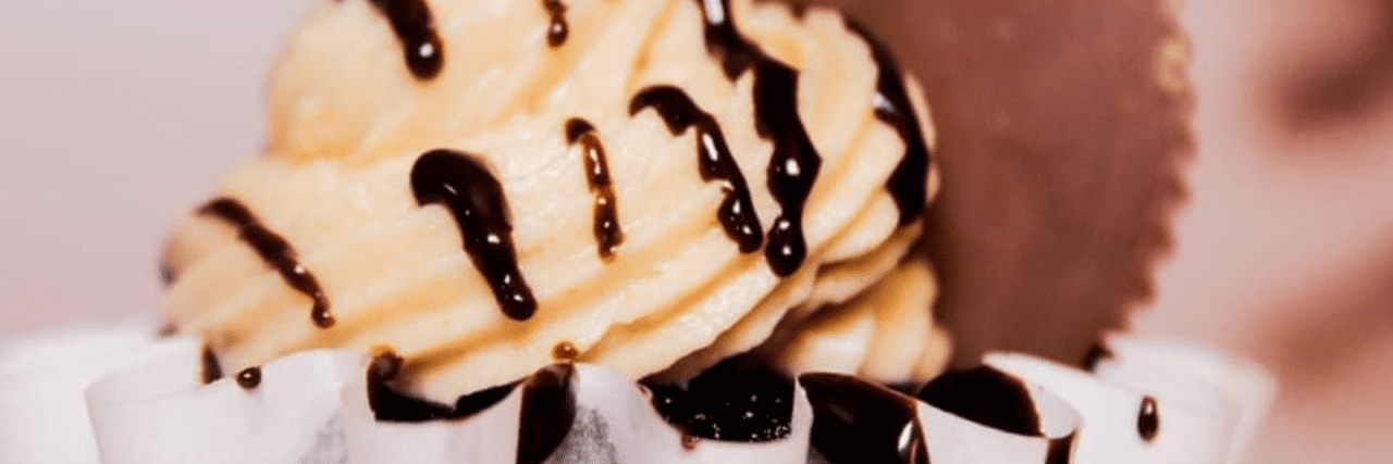 A close up shot of a chocolate cupcake with peanut butter frosting, chocolate drizzle, and a reese's cup on top.