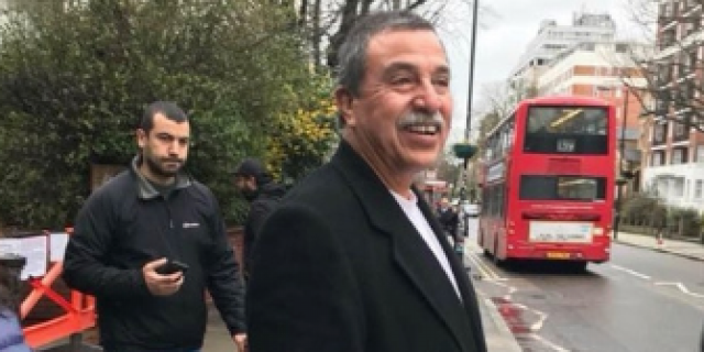 Image of Alfonso smiling and standing on sidewalk with a red double decker bus in the distance behind him