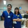 The author, a man with black hair and eyes wearing blue scrubs stands in the hospital alongside a woman in blue scrubs.