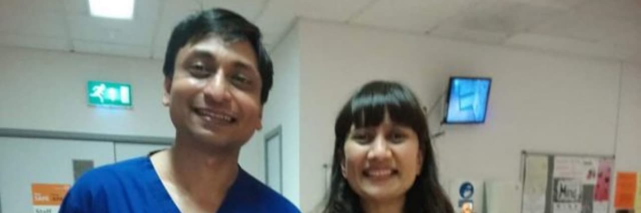 The author, a man with black hair and eyes wearing blue scrubs stands in the hospital alongside a woman in blue scrubs.
