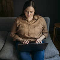 A woman with brown hair looks at her laptop and types.