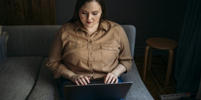 I'm a Health Writer, But It's OK That I Struggle to Take Pride in My Heath Conditions A woman with brown hair looks at her laptop and types.