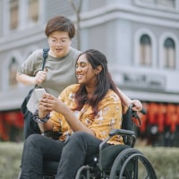 A woman in a wheelchair outside of a building chats with another woman.