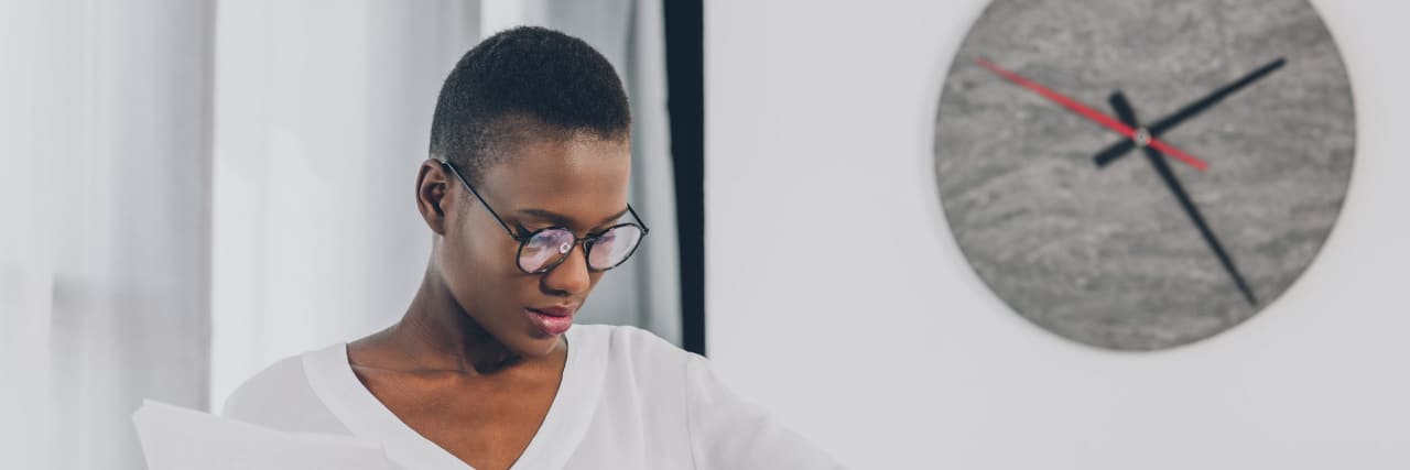 Why One Woman Prefers to Arrive Late With ADHD stylish african american businesswoman holding documents and checking time in office, clock on white wall