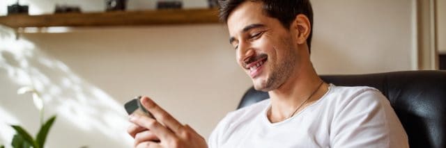photo of a man smiling and checking messages on his phone