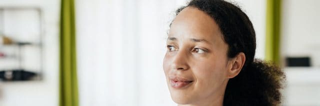 Woman of color at home looking to the side with a slight smile