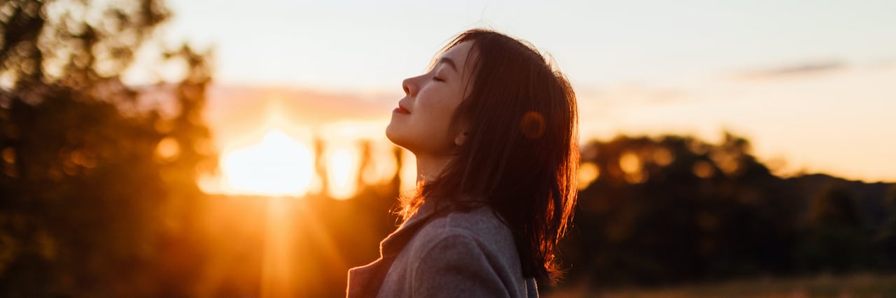 My DBT Toolkit Helps Me Regulate My Emotions With Borderline Personality Disorder Side portrait of woman with eyes closed inhaling fresh air, against sunset in the sky.