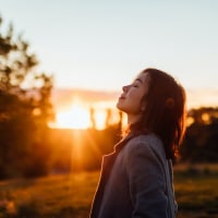 Side portrait of woman with eyes closed inhaling fresh air, against sunset in the sky.
