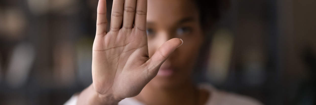 What to Know: Articles to Read Before Cutting Contact With an Abusive Parent photo of a woman out of focus, holding up her hand in front of camera to say stop