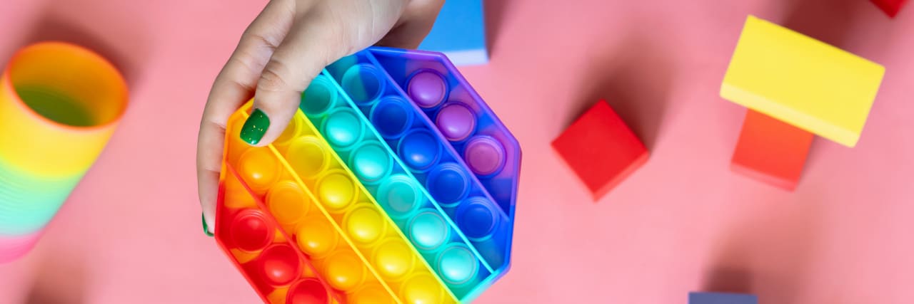 How to Stop Fidgeting With Anxiety photo of a person'a hand holding a rainbow-colored pop-it