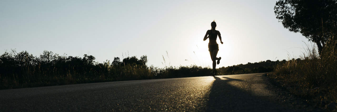 Signs You May Have an Exercise Compulsion and Possible Eating Disorder Silhouette of a woman in sportswear running on a rural road at sunset
