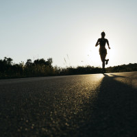 Silhouette of a woman in sportswear running on a rural road at sunset