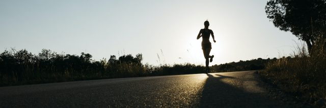 Silhouette of a woman in sportswear running on a rural road at sunset