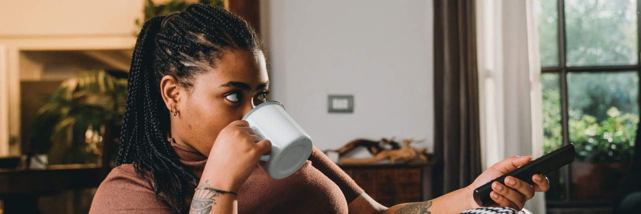 Dark skin woman is watching TV and drinking a coffee on the sofa