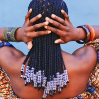 Rearview shot of a young woman wearing traditional African clothing and feeling her hair against a blue background