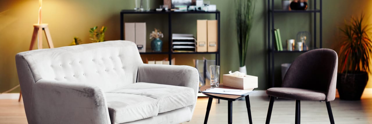 How Changes to a Therapist's Office Can Affect Trauma Patients Therapist's office with a gray sofa, small table, chair, lamp, bookshelf, and plants