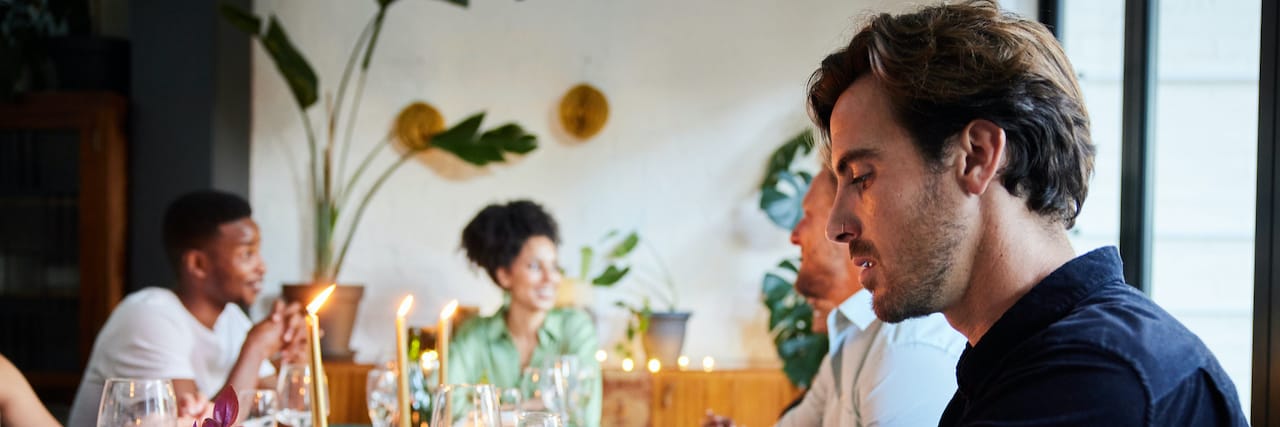 The Stress of Hosting a Party With Borderline Personality Disorder Man looking down at his phone while sitting at a table with friends