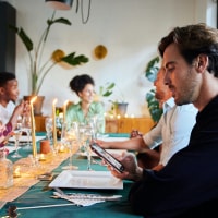 Man looking down at his phone while sitting at a table with friends