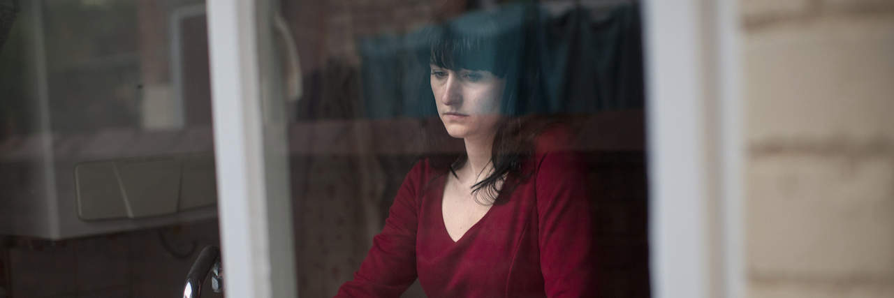 What It's Like to Lose a Neighbor to Suicide A woman with a sad expression on her face standing on front of her kitchen sink and looking out the window