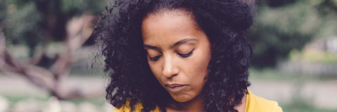 Grieving Tips When Losing a Child to Adoption Due to Mental Illness Woman in a yellow shirt sitting outside, looking down sadly