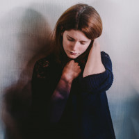 photo of a young person against a wall looking anxious with blurred figures all around