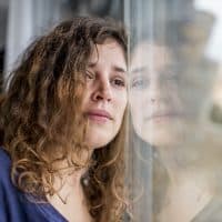 Woman with sad expression leaning against a window