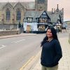 Photo of contributor, an Indian woman, standing in front of bridge and black and white Tudor building in England