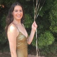 The author stands outside wearing a gold dress with spaghetti straps and holding pink and white balloons.