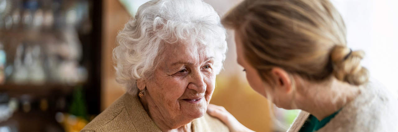 How Family and Caregivers Can Use Research to Help Dementia Patients Thrive A woman with blonde hair speaks to an elderly woman wearing a beige top.