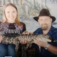 The author sits in a wheelchair next to her husband. They are jointly holding a gator.