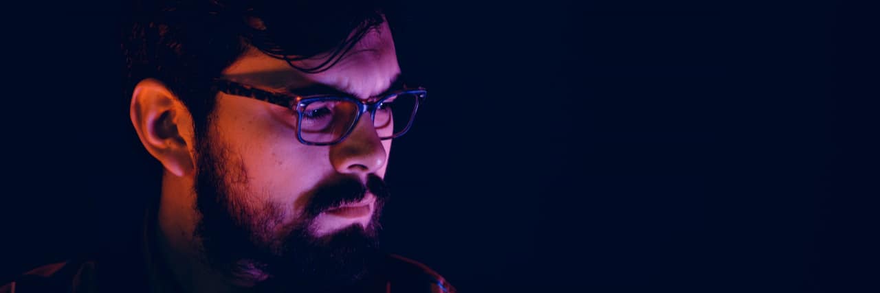 As a Survivor of Emotional Abuse, Is My Anger Healthy or Dangerous? Thoughtful man wearing glasses sitting in the dark looking away with a serious expression