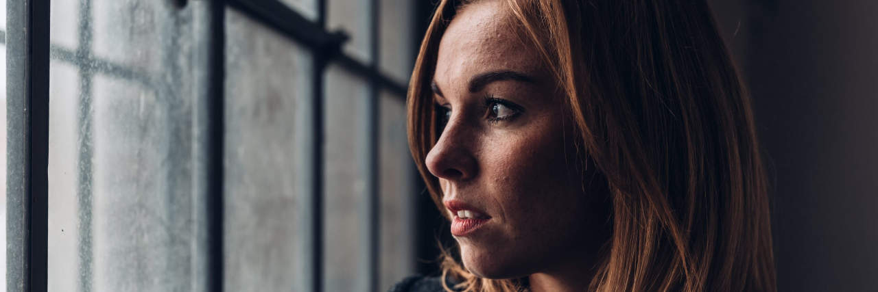Having Grief Triggers After Miscarriage and Pregnancy Loss A woman with red hair wearing a dark coat looks out a window.