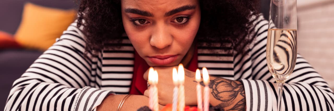 How to Celebrate a Bittersweet Birthday When You're Suicidal Depressive birthday. Cheerless unhappy woman looking at the candles while celebrating her birthday alone