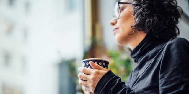Low angle shot of woman looking out of window with a coffee cup.