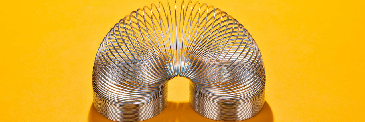 Ranking ADHD Stims Through the Eyes of a Neurotypical Curved Metal Coil Toy on Yellow Orange Colored Background High Angle View.