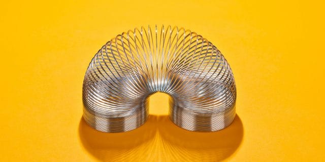 Curved Metal Coil Toy on Yellow Orange Colored Background High Angle View.