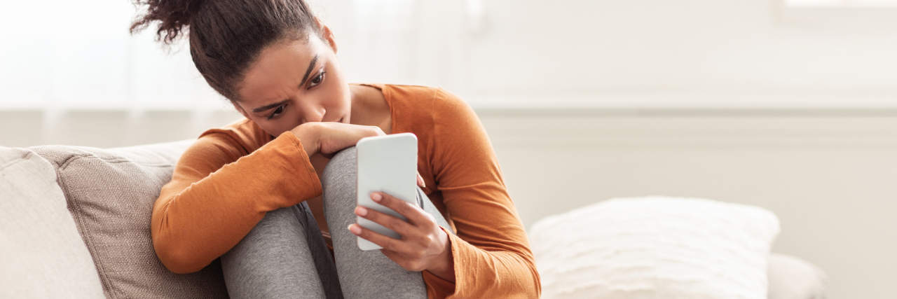 photo of a woman sitting on sofa looking at her phone, depressed