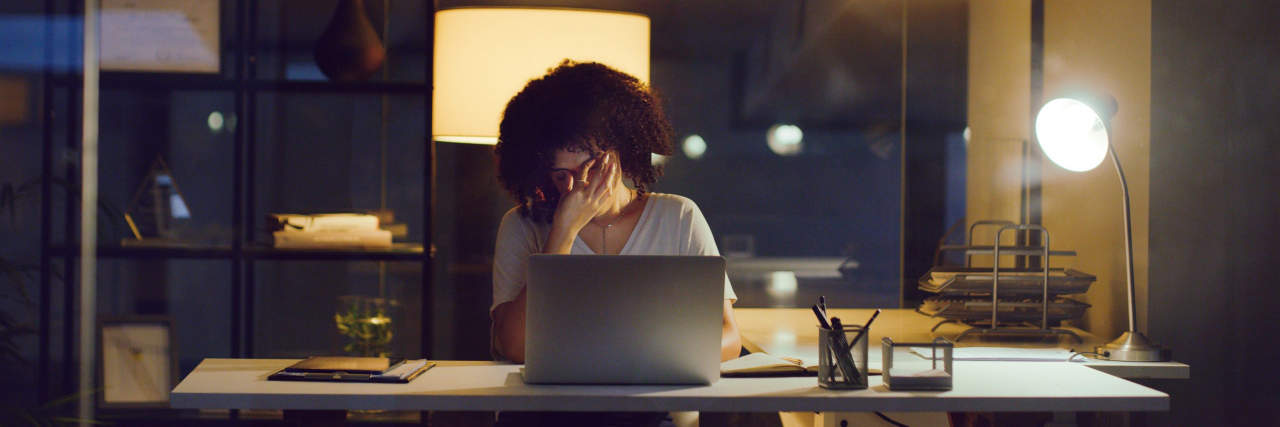 Shot of a young businesswoman looking stressed while using a laptop during a late night at work