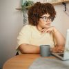 Large Black woman looking at computer with coffee mug at home
