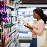 Pretty black lady with eco bag reading labels on food products, shopping for groceries at mall