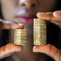 A Black woman holding two sets of coins one set that is larger and one is smaller