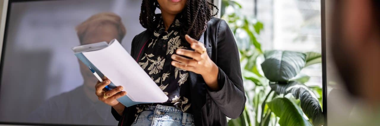 Why You Shouldn't Feel Bad for Job Hopping If You Have ADHD Young woman talking with team in a meeting. People having planning meeting in hybrid office, with colleagues joing via video call.