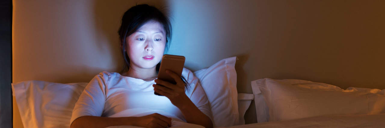 A Sexual Abuse Survivor’s Guide to Buying an Adult Toy Woman using a smart phone while in bed at night.