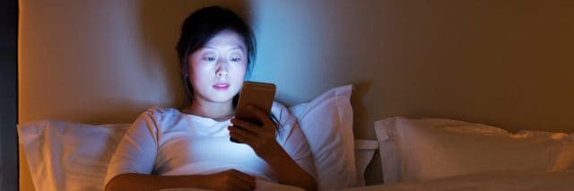 Woman using a smart phone while in bed at night.