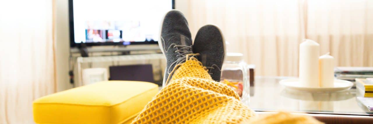 Essentials Every Depressed 30-Something Needs to Have Ready to Go Feet sticking out of blanket on couch in front of the TV